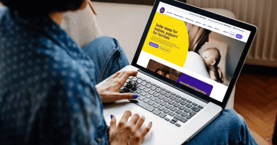 A person using a laptop to view the Lullaby Trust website.