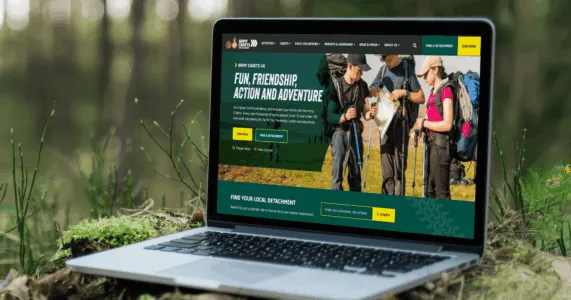 An open laptop in the forest, showing the Army Cadets homepage.